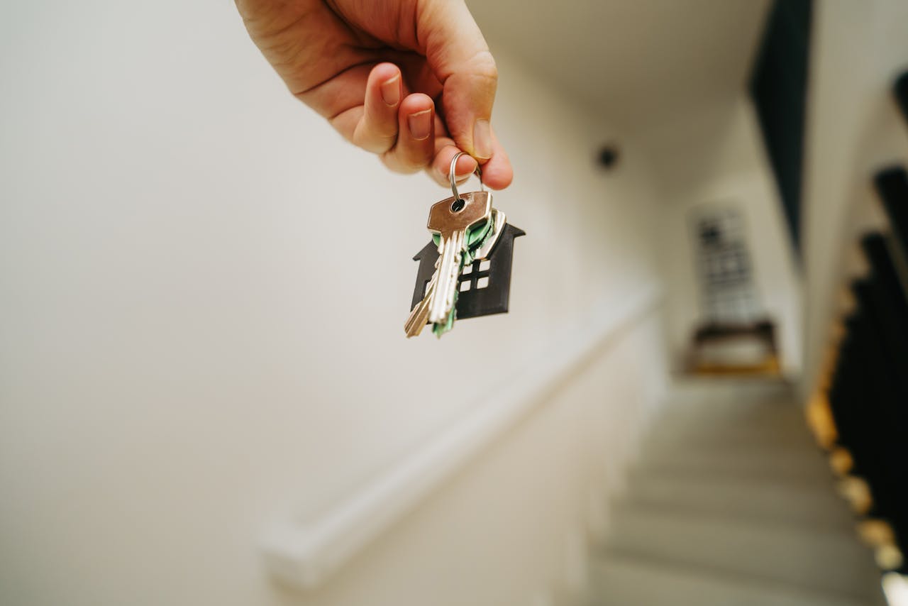 services-03 Close-up of a hand holding a keychain in the shape of a house, symbolizing real estate and property ownership.